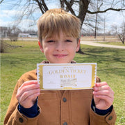 young boy holding up golden ticket scratch prize that says 'fudge brownie sundae after dinner!'